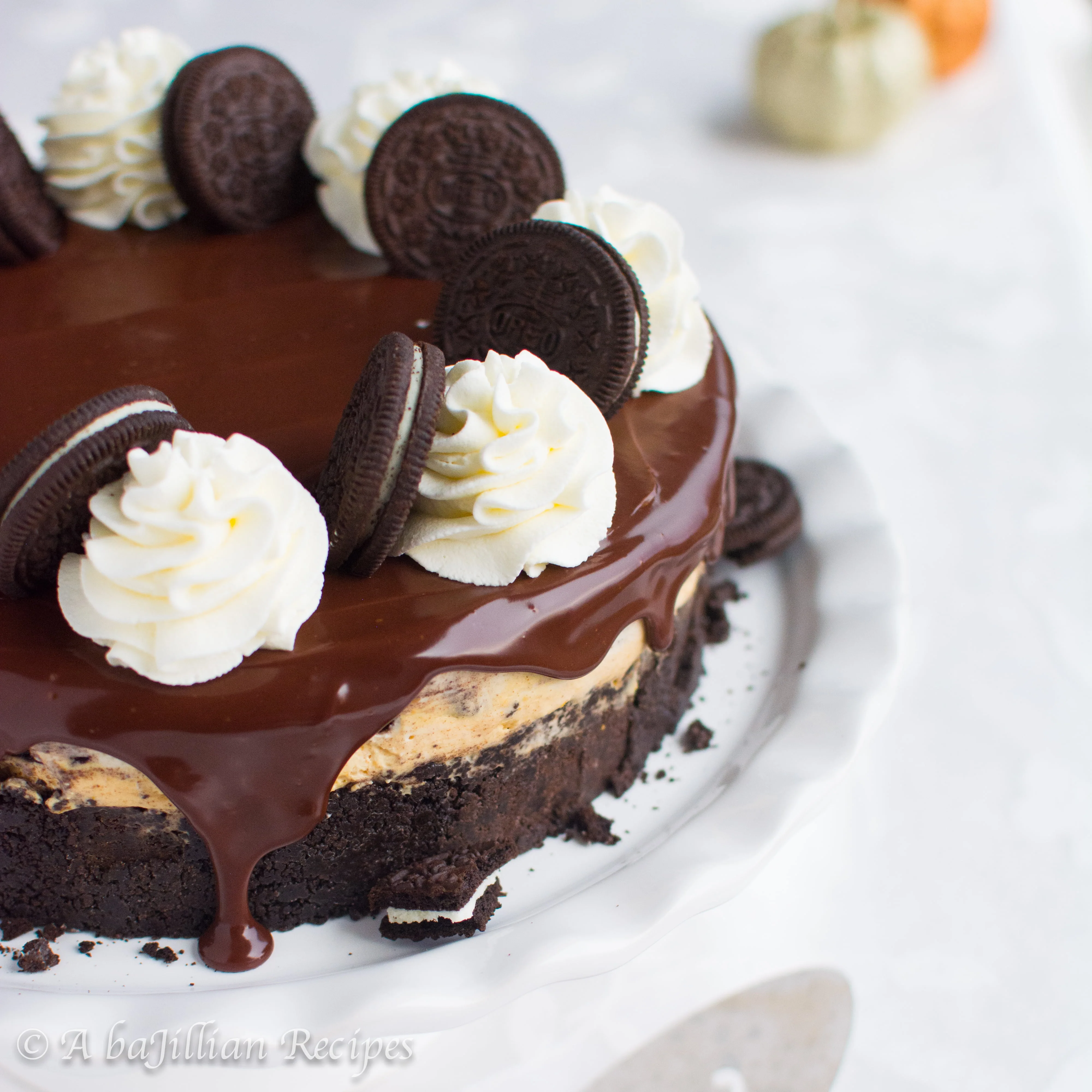 A simple no-bake cheesecake with a layer of creamy pumpkin cheesecake, a layer of Oreo-studded cheesecake, and enrobed in a rich chocolate ganache!