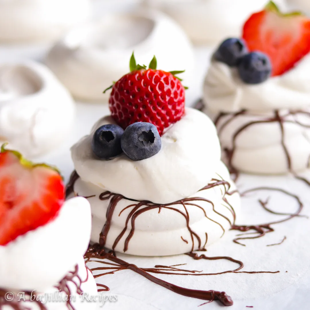 Melt-in-your-mouth meringues drizzled with dark chocolate, topped with a cloud of whipped cream and fresh berries! Naturally gluten-free!