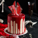 Moist layers of cocoa-kissed red velvet cake frosted with silky smooth vanilla Swiss meringue buttercream frosting! It's also drizzled in white chocolate ganache "blood" and adorned with "broken glass" sugar shards. A bloody good cake indeed!