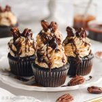 Moist chocolate cupcakes crowned with a silky smooth caramel Swiss meringue buttercream, topped with toasted pecans, and drizzled in both chocolate ganache and rich caramel!